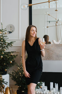 Stylish young woman in a black dress holds a glass of champagne in her hands and celebrates