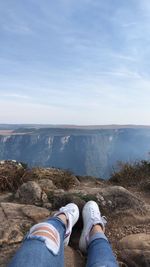 Low section of woman sitting on mountain against sky