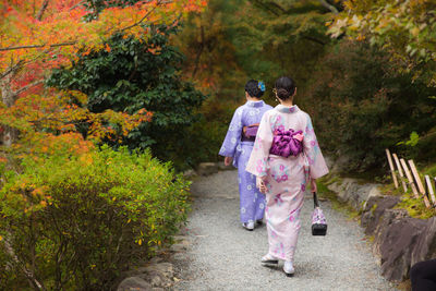 Rear view of women walking on footpath by trees