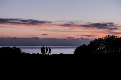 Silhouette people standing on beach against sky during sunset