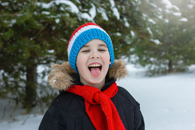 Funny boy in winter clothes and a red scarf catches snowflakes with his tongue