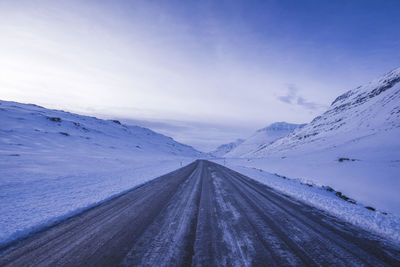 Road amidst snowcapped mountains against sky during winter