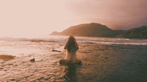 Woman standing on beach against sky during sunset