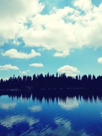 Silhouette trees by lake against sky