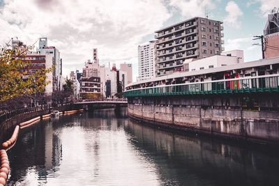 Bridge over river by buildings in city against sky