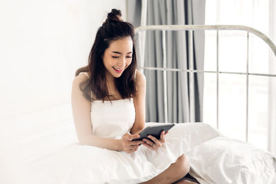 Young woman using mobile phone while sitting on bed