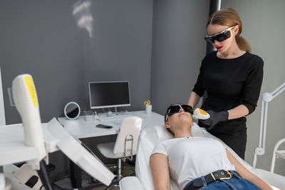 Young caucasian woman in goggles on photorejuvenation procedure. doctor cosmetologist with a female