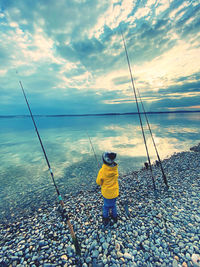 Rear view of man fishing in sea against sky