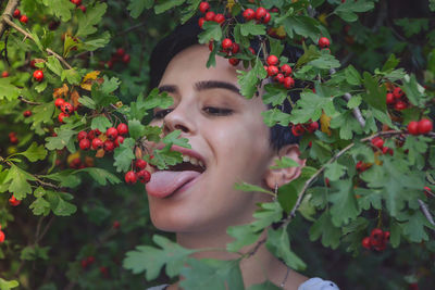 Close-up of young woman eating red berries on plant