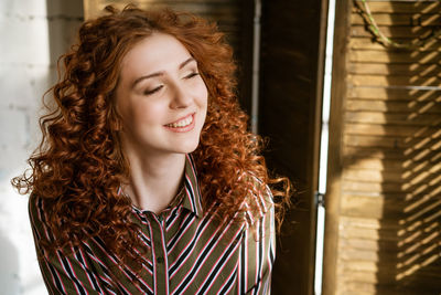 Portrait of happy redhead young woman near window