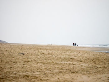 People walking on sand dune on the beach against clear sky