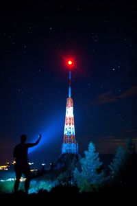 Silhouette man standing by illuminated tree against sky at night