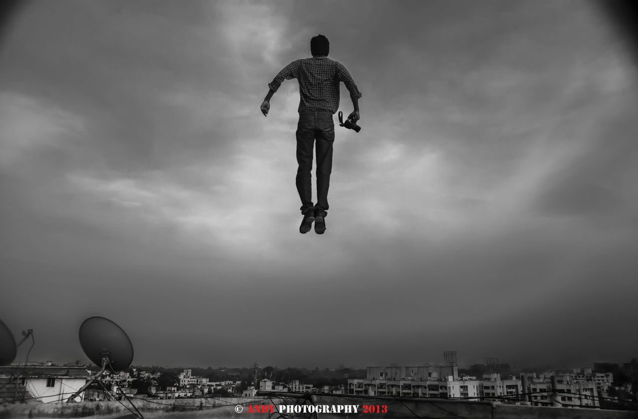 FULL LENGTH OF MAN JUMPING OVER CITYSCAPE AGAINST SKY