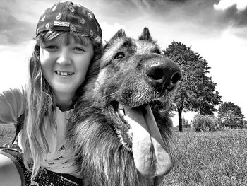 Portrait of smiling girl with dog on grassy field against sky