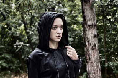 Thoughtful young woman wearing hooded shirt against trees