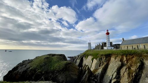 Lighthouse amidst sea and buildings against sky