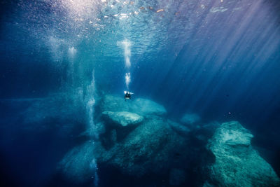 Man scuba diving by rock formation in sea at gozo