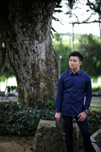 Young man standing by tree in forest