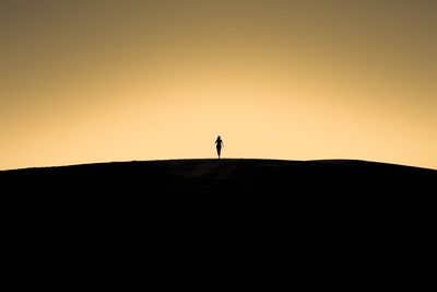 Silhouette man standing on rock against sky during sunset