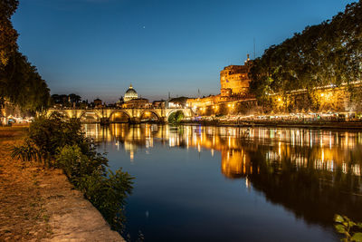 Illuminated buildings by lake against sky