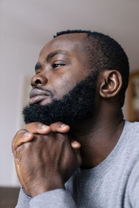 Thoughtful bearded man with hands clasped on chin looking away at home