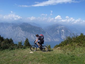 Man riding bicycle on field against mountains