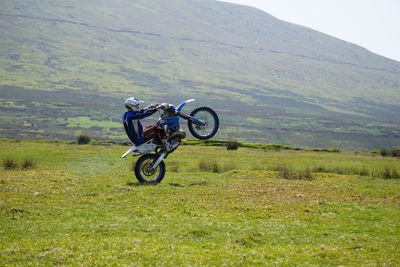 Motocross rider performing stunt on field by mountain