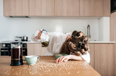 Sleepy woman with food spreaded on table at home