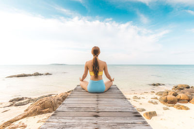 Rear view of woman doing yoga on jetty at beach