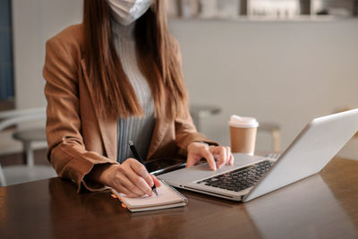 Midsection of woman using mobile phone while sitting on table