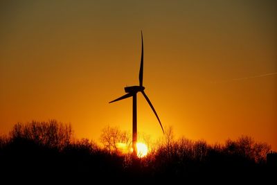 Silhouette of wind turbines on field against romantic sky