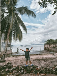 Rear view of kid with arms outstretched on beach against sky