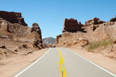 Road amidst rocky mountains against clear sky on sunny day