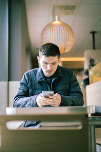 A young man with a phone in his hands is sitting in a diner.