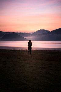 Rear view of woman standing by lake during sunset