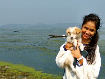 Portrait of dog holding hands by sea against sky