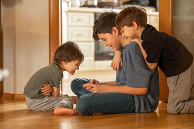 Side view of boy sitting on hardwood floor at home