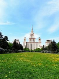 View of building and plants on field against cloudy sky