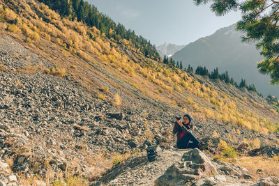 Woman photographing while sitting on mountain during sunny day