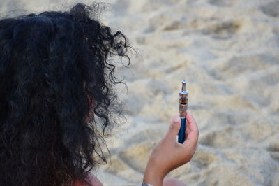Rear view of woman holding electronic cigarette at beach