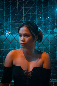 Portrait of young woman looking away while standing against wall