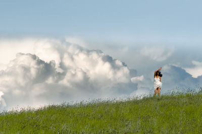 Asian woman in white dress on meadow frozen in motion against clouds