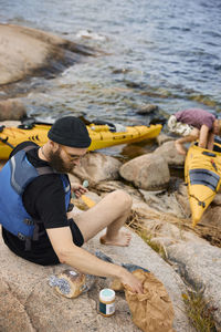 High angle view of man sitting at sea near kayak and preparing food