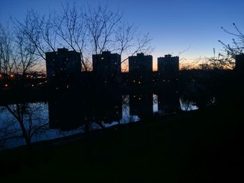 Silhouette buildings by lake against sky at night