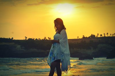 Woman standing on beach against sky during sunset