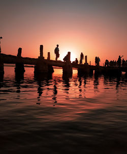 Silhouette people on lake against sky during sunset