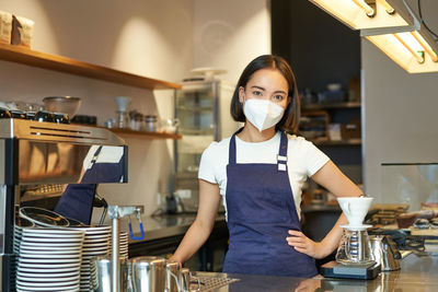 Portrait of young woman wearing mask while standing in cafe