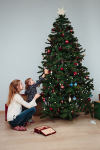 Siblings decorating christmas tree against wall at home