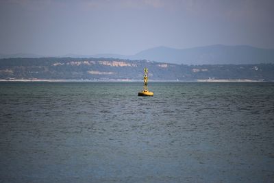 Distant view of buoy floating in sea against sky