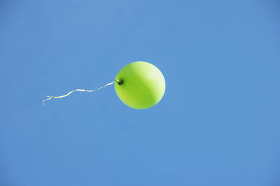 Low angle view of green helium balloon flying against clear blue sky